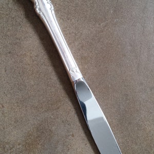 May include: A silver butter knife with an ornate handle. The knife has a sharp blade and a polished finish.