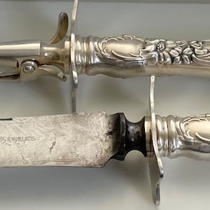 Puede incluir: Un juego de trinchar de plata con un cuchillo y un tenedor. Los mangos están adornados con diseños florales.