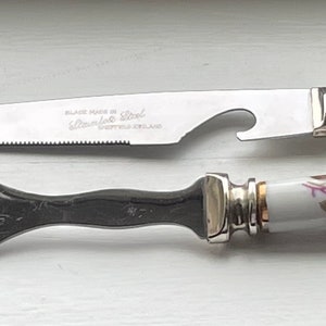 May include: A set of two kitchen utensils with floral patterned handles. The knife has a serrated blade and a bottle opener. The fork has two prongs.