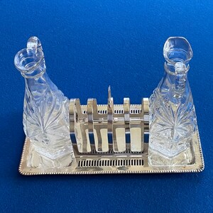 May include: A silver serving tray with two clear glass decanters with a starburst pattern. The decanters have a silver metal rack in between them.