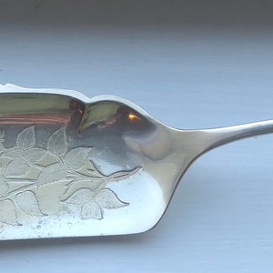 以下が含まれることがあります： 装飾的な花柄の銀製のバターナイフ。ハンドルは繰り返しのパターンで飾られています。