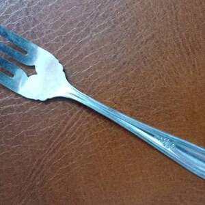May include: A silver fork with a decorative handle. The fork has four tines and a slightly curved handle.