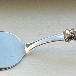 May include: A silver cake server with a white pearlescent handle. The handle has a decorative silver design at the end.