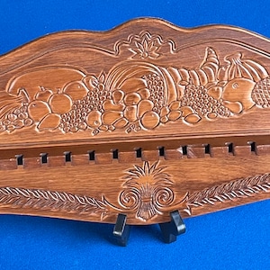 May include: A wooden wall-mounted knife holder with a carved fruit design. The holder has 16 slots for knives and a decorative pineapple design at the bottom.