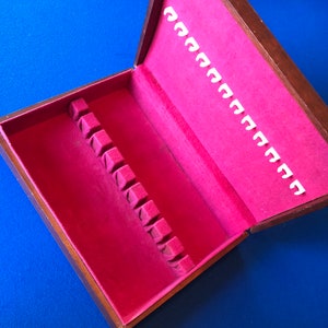 Puede incluir: Una caja de madera con un interior de terciopelo rojo y ranuras para cubiertos. La caja está abierta y las ranuras están vacías.