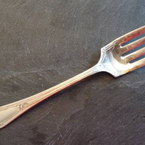 May include: A silver fork with a decorative handle. The fork has four tines and is on a dark gray background.