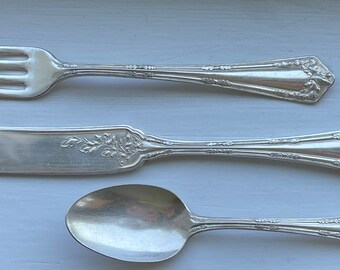 May include: A set of three silver-plated utensils, including a fork, butter knife, and spoon. The utensils have an ornate design with floral motifs.