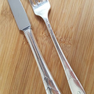 Könnte beinhalten: Ein silbernes Messer und eine Gabel mit verzierten Griffen. Beide Teile haben den Buchstaben "B" in den Griff graviert.
