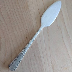 May include: A silver butter knife with an ornate handle. The blade is smooth and pointed.