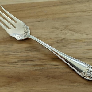 Può includere: Una forchetta d'argento con un motivo floreale sul manico. La forchetta è su una superficie di legno.