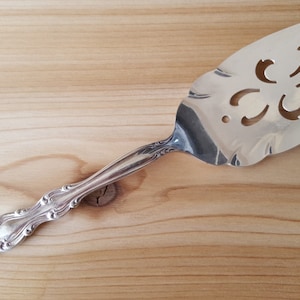 Può includere: Servitore per torta d'argento con un designo ornato e decorativo sul manico e un designo decorativo ritagliato sulla lama.
