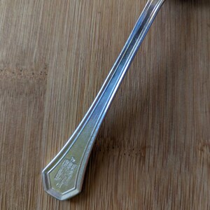 May include: A silver spoon with a decorative handle. The handle has a raised design with the words "The Gorham Co. Sterling" and "1924" inscribed on it.