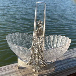 May include: A silver and glass serving basket with a decorative handle and a scalloped bowl. The basket has a delicate, intricate design and is perfect for serving fruit or other treats.