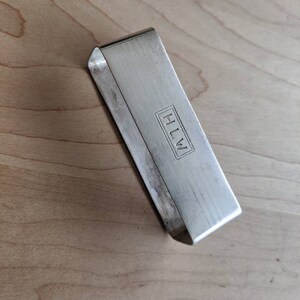 Peut inclure: Bague à serviette en argent de forme rectangulaire avec une surface texturée. La bague porte les initiales "HLW" gravées.