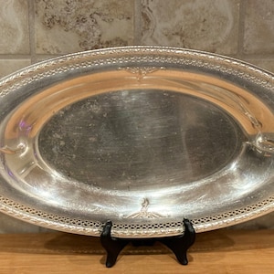 Può includere: Un vassoio da portata ovale in argento con un bordo decorativo e un design in rilievo sul bordo. Il vassoio è vuoto e ha una finitura lucida.