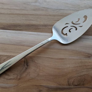 May include: A silver cake server with an ornate, cut-out design. The handle is decorated with a floral pattern.