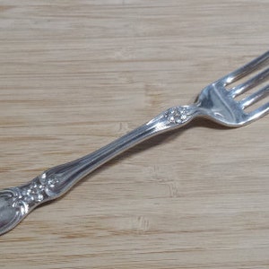 Könnte beinhalten: Eine silberne Gabel mit einem verzierten Griff. Der Griff hat ein Blumenmuster.