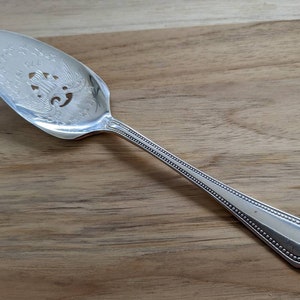 May include: Silver serving spoon with a decorative design of an eagle and stars. The spoon has a beaded handle.