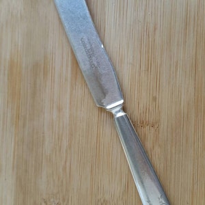 Puede incluir: Un cuchillo de mantequilla de plata con un diseño decorativo en el mango. El cuchillo tiene las palabras "Wm Rogers & Son" y "1847 Rogers Bros." grabadas en la hoja.