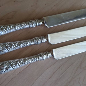 Może przedstawiać: Trzy srebrne noże do masła z ozdobnymi uchwytami w kształcie winorośli.