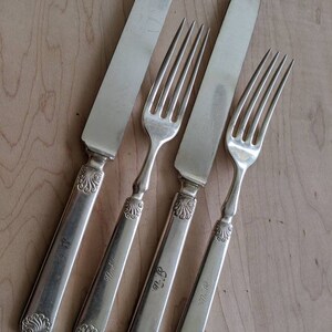 May include: Four pieces of silverware, including two knives and two forks, with ornate handles. The handles are engraved with the initials "M.B."