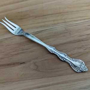 Può includere: Una forchetta d'argento con un manico decorato. La forchetta ha un design decorativo con un motivo floreale.