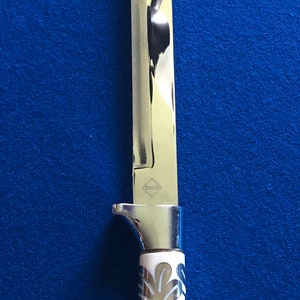 May include: A silver knife with a white handle featuring a decorative leaf pattern. The blade is long and thin, and the handle has a silver cap at the end.