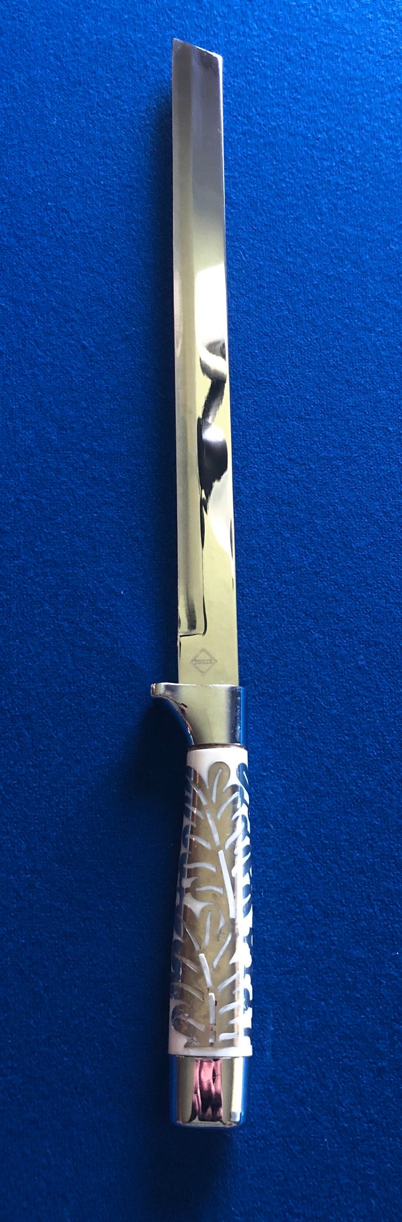 May include: A silver knife with a white handle featuring a decorative leaf pattern. The blade is long and thin, and the handle has a silver cap at the end.
