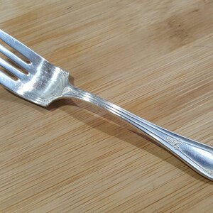 May include: A silver fork with a decorative handle. The fork has four tines and a slightly curved handle.