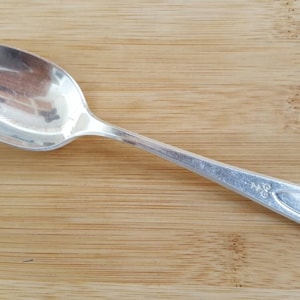 May include: A silver spoon with a rounded bowl and a long, slender handle. The handle has a decorative design and the words "18/8" engraved on it.