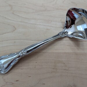 May include: A silver ladle with an ornate handle. The ladle has a rounded bowl and a long, slender handle with a decorative design.