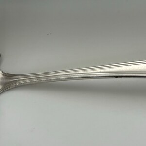 May include: A silver ladle with a rounded bowl and a long, curved handle. The handle has a decorative design.