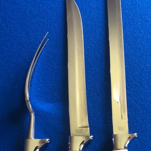 May include: Three silver kitchen utensils, including a fork, a long knife, and a shorter knife. The knives have the text "Stainless Solingen Germany" on the blades.