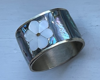 May include: A silver and abalone shell napkin ring with a white flower design.