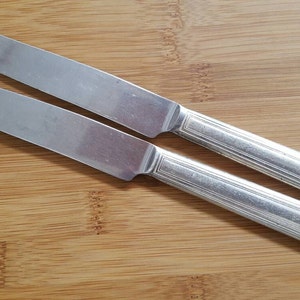 May include: Two silver metal dinner knives on a wooden surface.