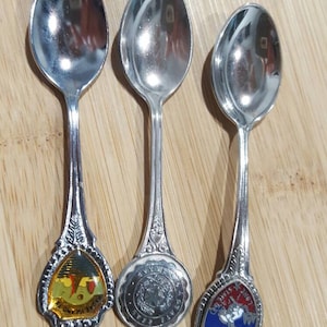 May include: Three silver souvenir spoons with colorful enamel designs. The spoons feature images of "Isle of Man", "State of Texas", and "The Lone Star State".