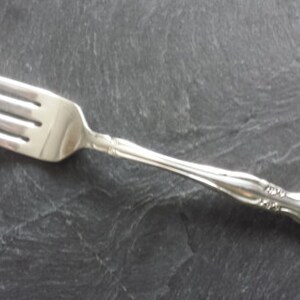 May include: A silver fork with an ornate handle. The fork has four tines and a polished finish.