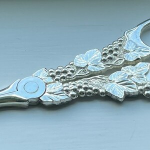May include: Silver-plated scissors with a grapevine design. The handles are decorated with leaves and grapes.