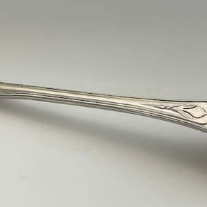 May include: A silver teaspoon with a rounded bowl and an ornate handle. The handle is decorated with a floral design.