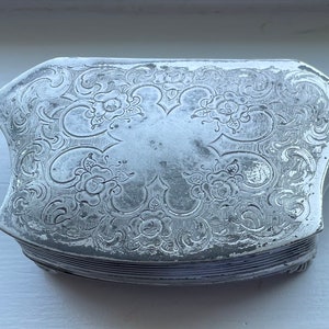 Könnte beinhalten: Eine silberne, verzierte, Scharnierbox mit einem floralen Design. Die Box ist geschlossen und scheint aus mehreren Schichten zu bestehen.