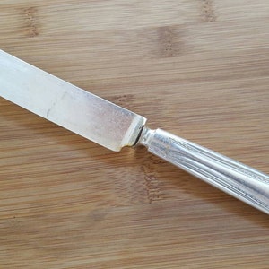 Puede incluir: Un cuchillo de mantequilla de plata con un mango adornado y el número "121" grabado en el lateral.