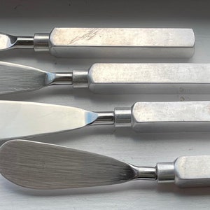 Può includere: Quattro spalma burro in acciaio inossidabile. Ogni spalma burro ha una lama ampia e curva e un manico rettangolare. Le lame hanno una finitura spazzolata e i manici sono solidi e metallici. Progettati per servire burro o altre creme spalmabili.