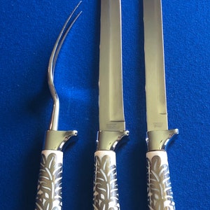 May include: Three silver kitchen knives with white handles featuring a floral design. The knives have stainless steel blades and are arranged vertically on a blue background.