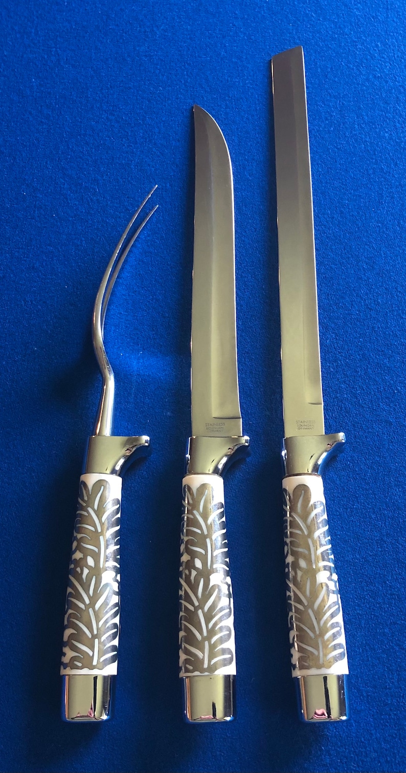 May include: Three silver kitchen knives with white handles featuring a floral design. The knives have stainless steel blades and are arranged vertically on a blue background.