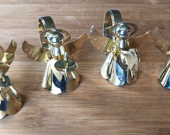 Könnte beinhalten: Vier goldene Engel-Serviettenringe. Jeder Engel hält ein Musikinstrument. Die Engel stehen auf einer Holzoberfläche.