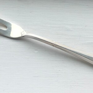 May include: A silver serving fork with a decorative handle. The fork has two prongs and a long, slender handle.