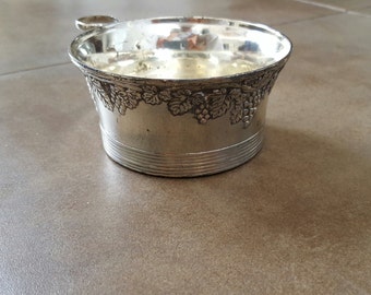 Puede incluir: Enfriador de vino de plata con un diseño de vid alrededor del borde superior. El enfriador tiene un asa en el lateral.