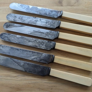 May include: Set of seven vintage knives with ivory handles and silver blades. The blades are worn and have a patina. The handles are smooth and have a slight yellow tint.