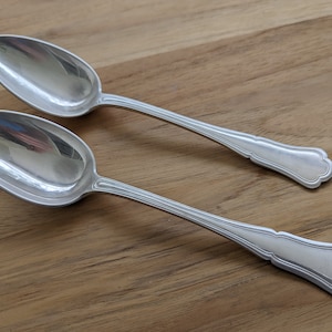 May include: Two silver spoons with ornate handles on a wooden surface.