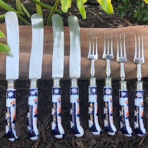 May include: Set of eight silver-plated cutlery pieces with blue and white porcelain handles featuring a floral design. The handles have gold accents. The set includes five butter knives and three forks.